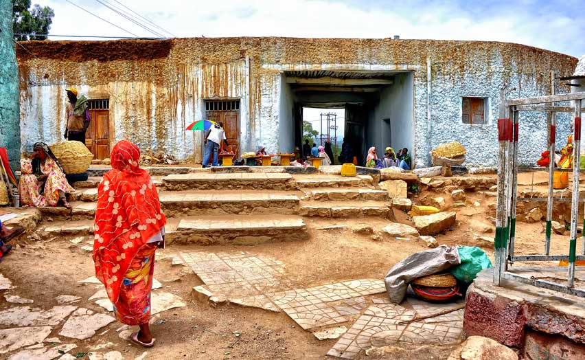 One of the gates through the wall of Harar Jugol, Ethiopia, with people and baskets on the worn stone steps in front of it.