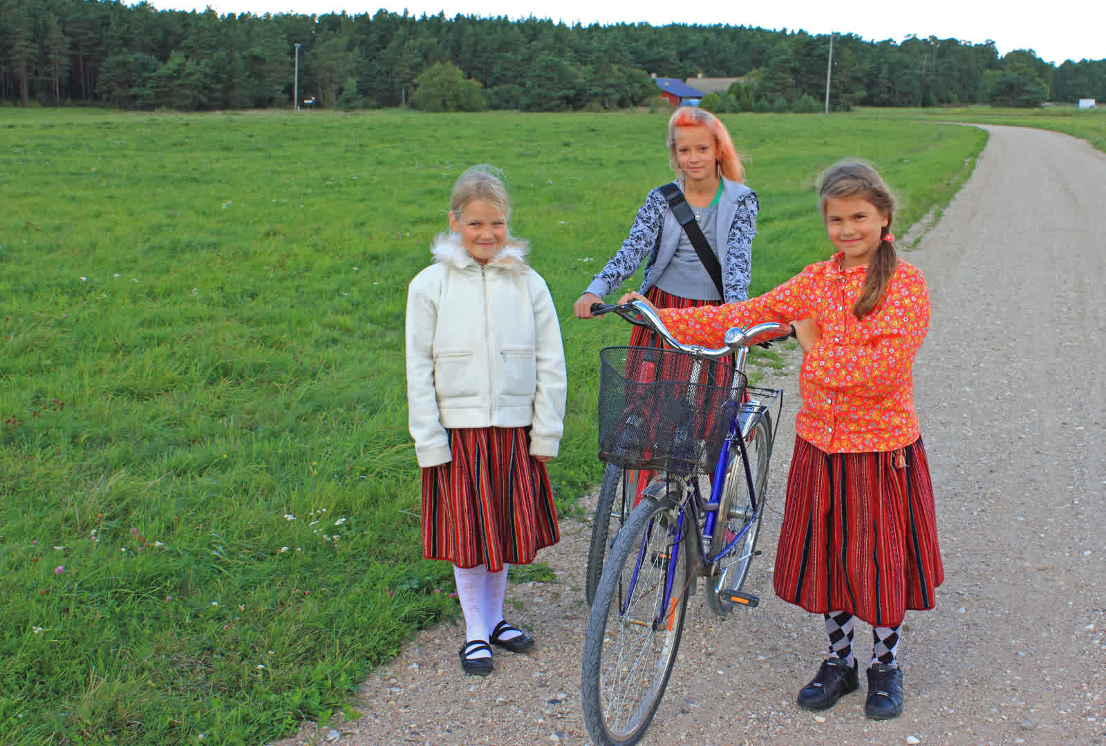 Two girls in red striped Kihnu wool skirts walking home along a village road on the first day of school.